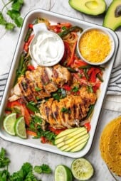 Overhead view of chicken fajitas in pan with bowls of sour cream and cheese
