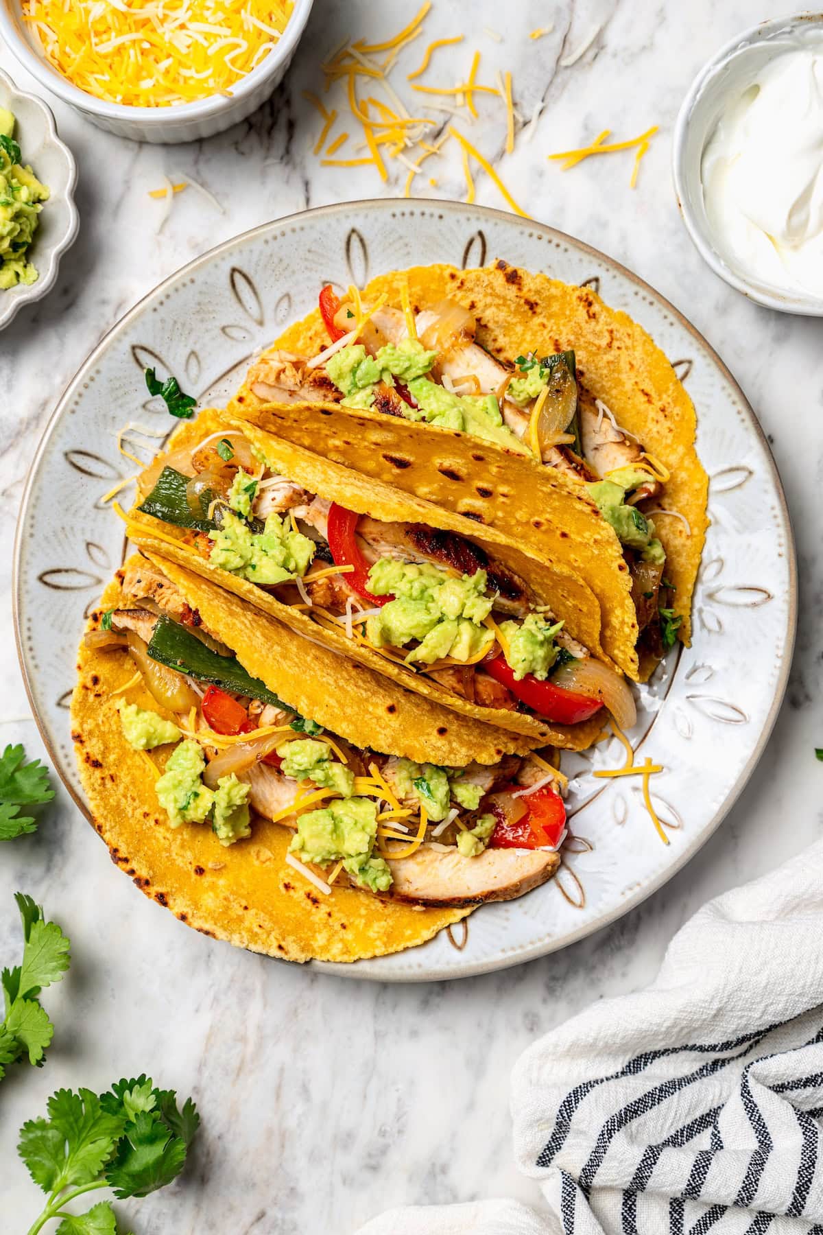 These easy chicken fajitas are made with grilled chicken breast, bell peppers and onions and served sizzling hot with tortillas and cheese! Overhead view of chicken fajitas in tortillas on plate