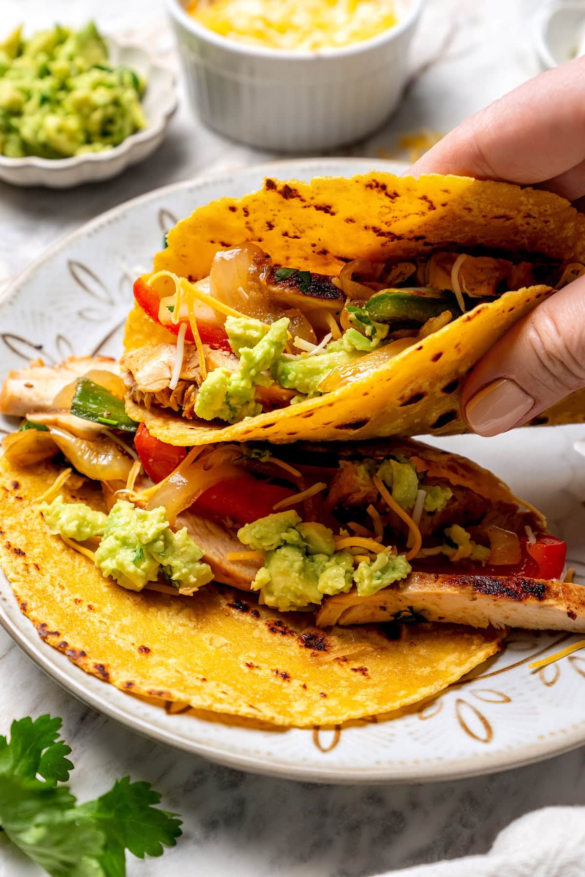 These easy chicken fajitas are made with grilled chicken breast, bell peppers and onions and served sizzling hot with tortillas and cheese! Hand picking up chicken fajitas wrapped in corn tortilla