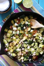 Mexican zucchini in a black cast iron skillet with a wooden spoon.