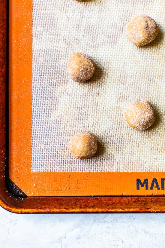 A simple sugar cookie dough is rolled in sugar and pumpkin pie spice to make these soft and chewy Pumpkin Snickerdoodles. Balls of pumpkin snickerdoodles on a baking sheet