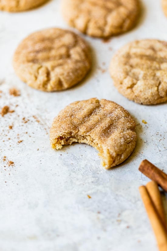 A simple sugar cookie dough is rolled in sugar and pumpkin pie spice to make these soft and chewy Pumpkin Snickerdoodles. Pumpkin snickerdoodle cookies on a counter, one half eaten