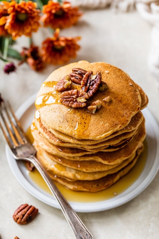 Made with whole wheat flour, pumpkin puree, pumpkin spice, and pecans, these Pumpkin Pancakes are soft, fluffy, and filled with fall flavor. Overhead view of a tall stack of pumpkin pancakes