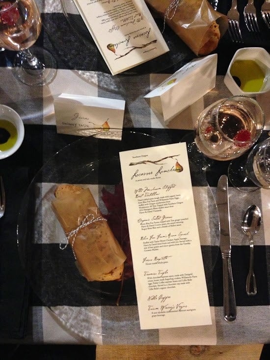 A place setting with clear glass plate, with a piece of bread wrapped in brown paper and a menu