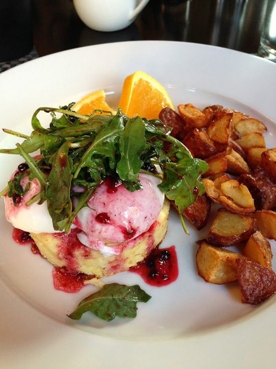 Poached eggs over souffle with arugula salad and berry dressing, a side of roasted potato chunks, and orange slices