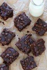 Overhead view of black bean brownies on parchment paper with glass bottle of milk