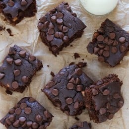 Overhead view of black bean brownies on parchment paper with glass bottle of milk