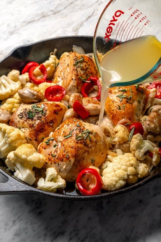 Cauliflower and chicken breasts make this Chicken Scarpariello recipe low carb, but it's just as spicy and flavorful as the classic version! Pouring broth into pan of chicken scarpariello.