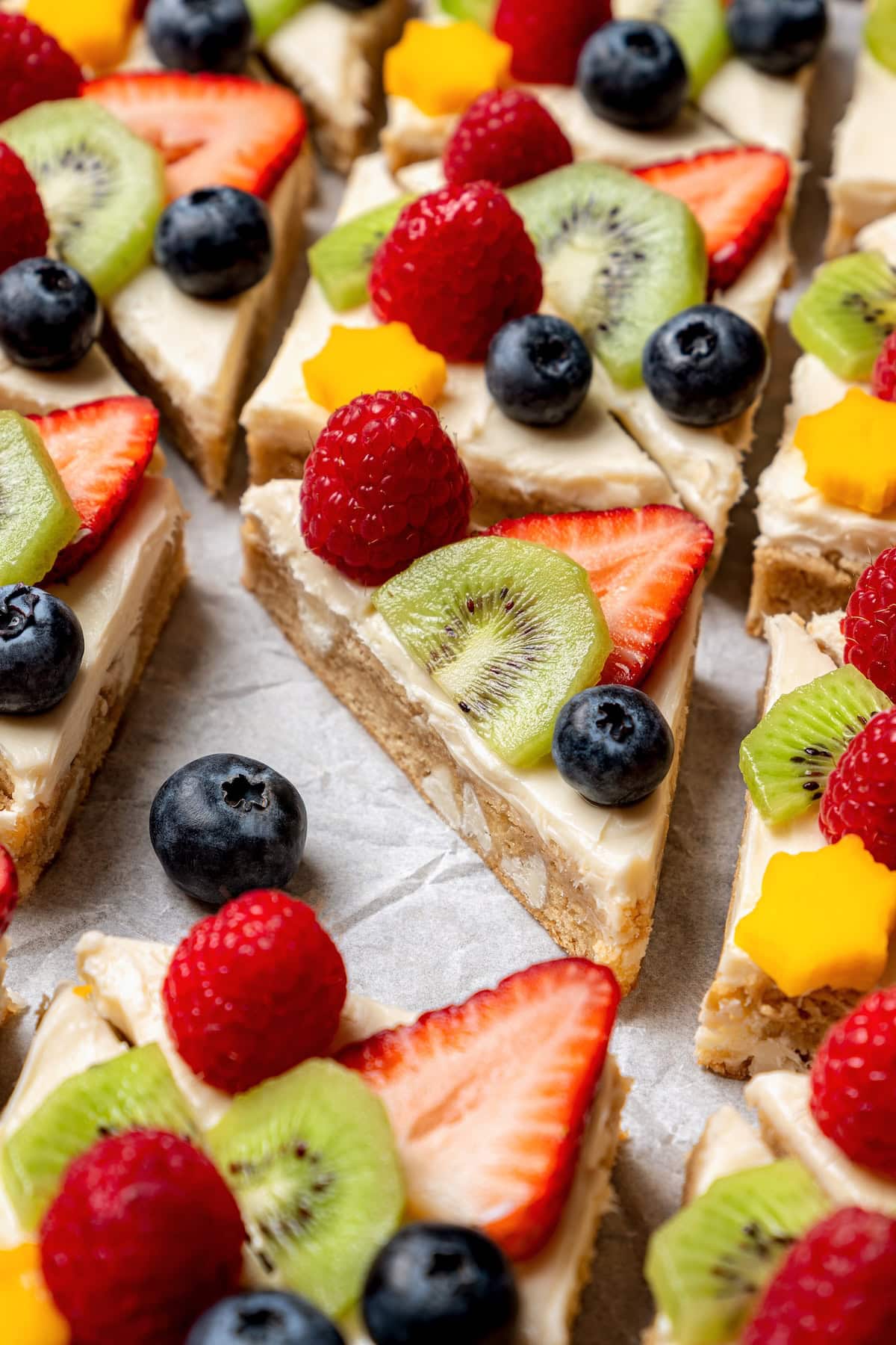 This easy fruit pizza is made with a lightened-up sugar cookie crust and topped with fluffy cream cheese frosting and colorful fresh fruit! Sugar cookie fruit pizza on sheet pan