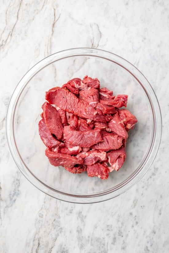 This lightened up Peruvian lomo saltado recipe is packed with flavor, with tender sirloin and veggies served alongside crispy baked fries. Overhead view of beef in glass bowl