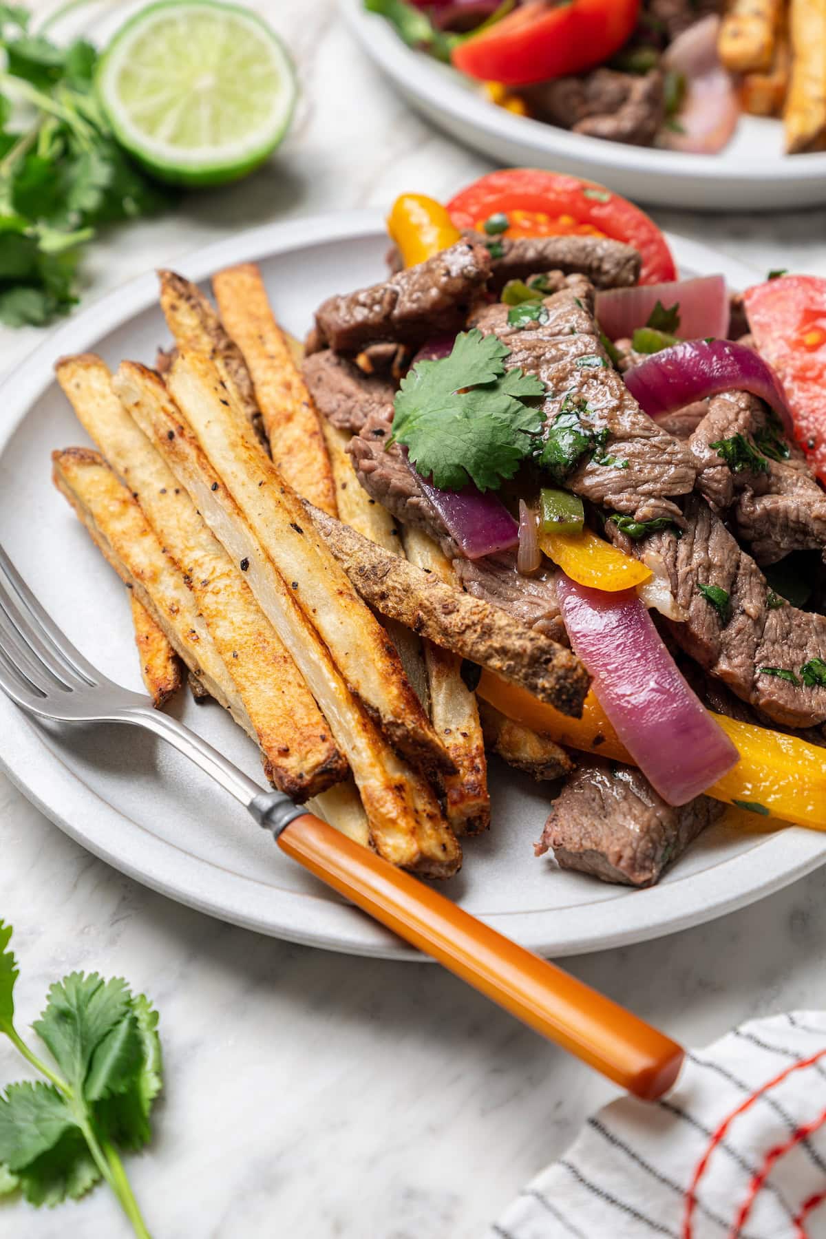 This lightened up Peruvian lomo saltado recipe is packed with flavor, with tender sirloin and veggies served alongside crispy baked fries. Lomo saltado beef stir fry on plate with fork