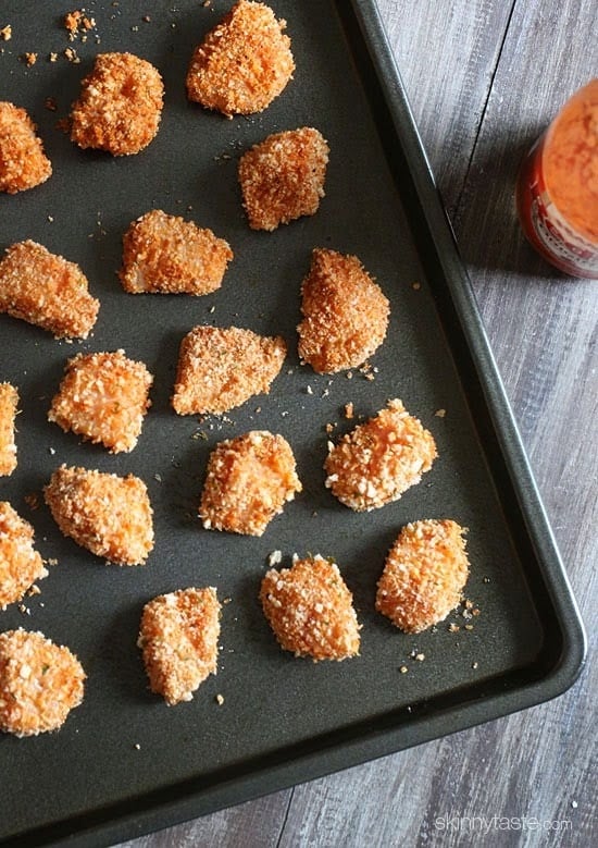 A baking sheet with uncooked breaded chunks of chicken.