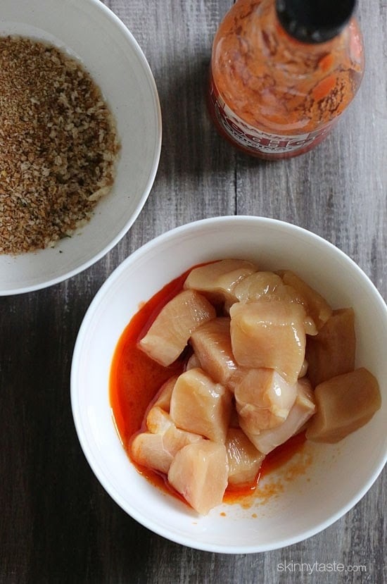 A bowl of cubed raw chicken with hot sauce and a bowl of breading mixture.
