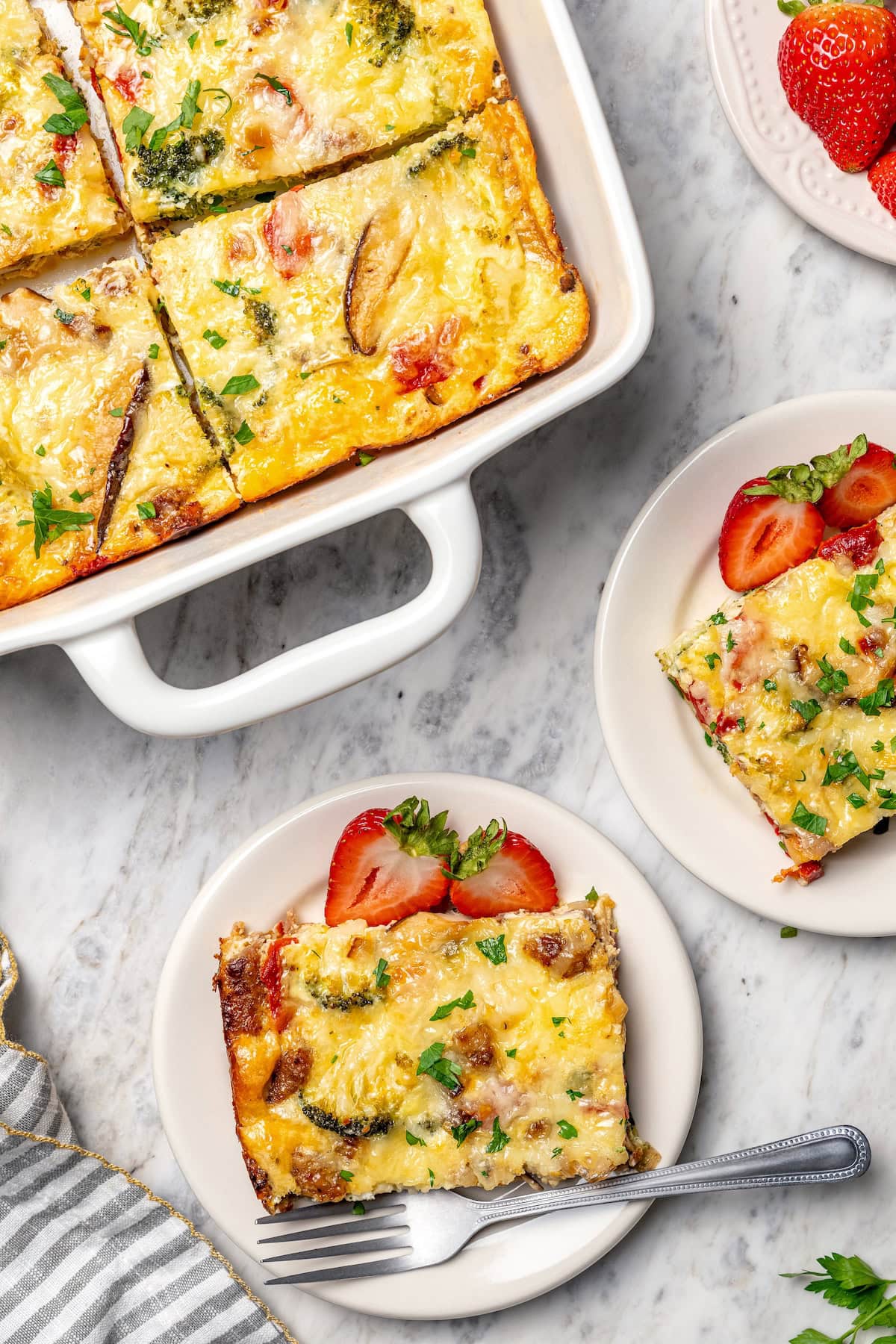 This healthy breakfast casserole recipe with sausage, cheese and veggies is hearty, flavorful, and perfect for meal prep or a weekend brunch! Two plates of breakfast casserole set next to baking dish.