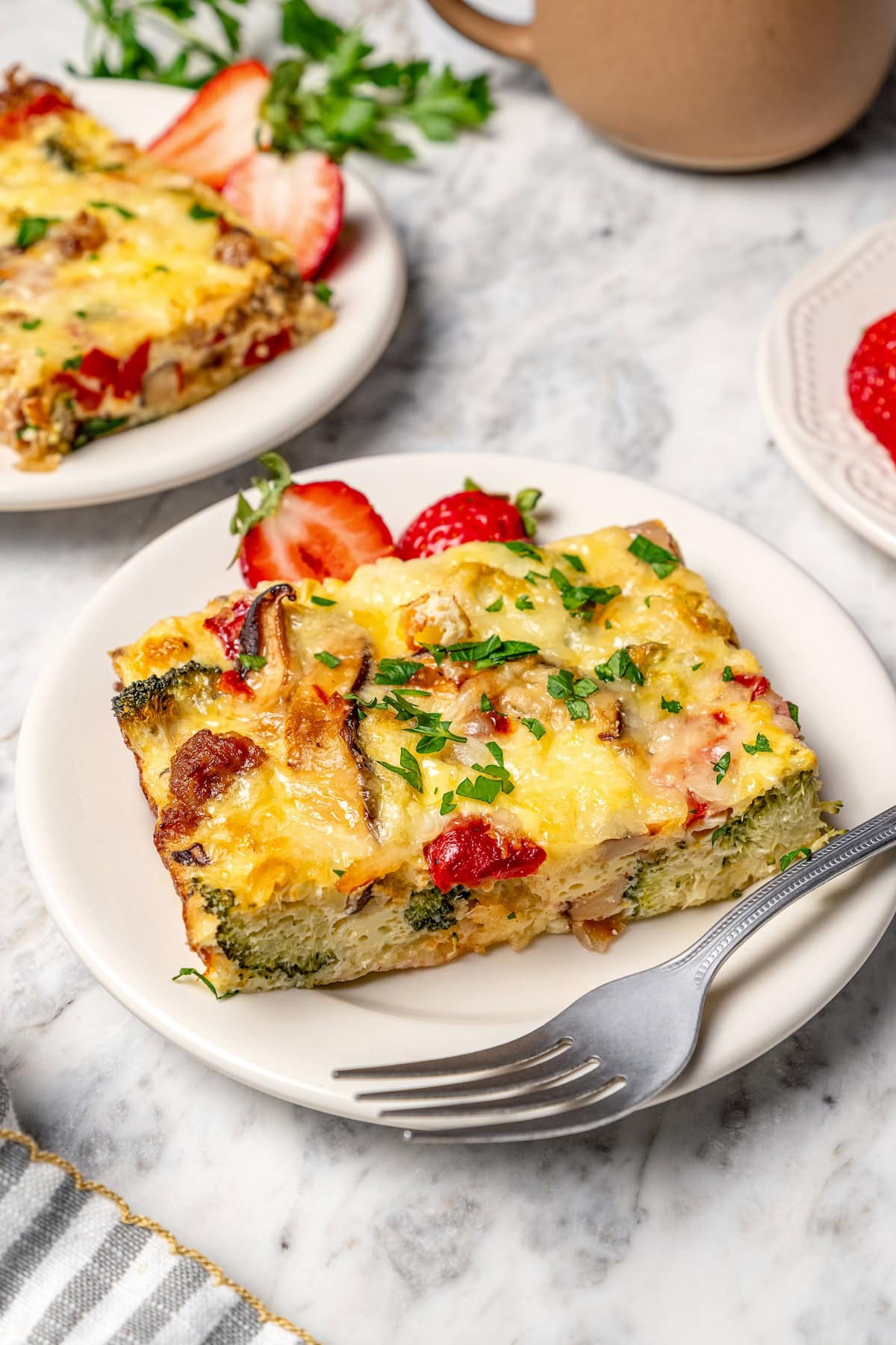 This healthy breakfast casserole recipe with sausage, cheese and veggies is hearty, flavorful, and perfect for meal prep or a weekend brunch! Slice of breakfast casserole on plate with fork.