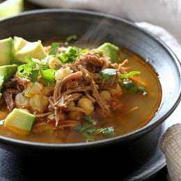 Bowl of pozole rojo with avocado and cilantro for garnish.