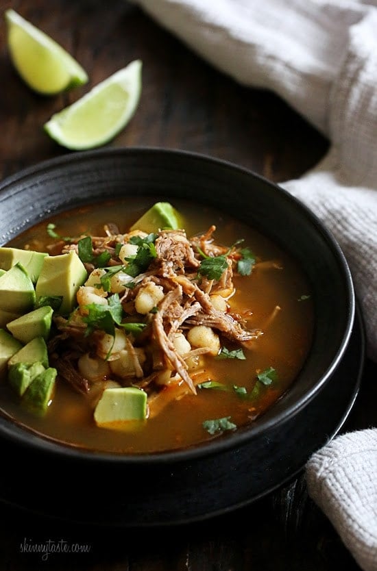 This Instant Pot Pozole Rojo recipe is easier and faster than the classic version! With pork, hominy and spices, it's hearty and flavorful. Bowl of pozole rojo with avocado and cilantro for garnish and lime wedges in background