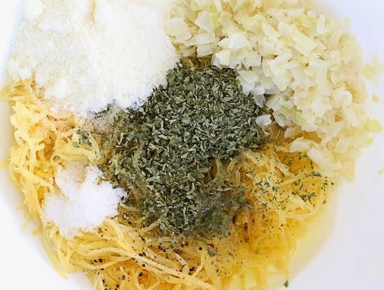 A mixing bowl with cooked spaghetti squash, diced onion, grated Pecorino Romano cheese, and dried herbs