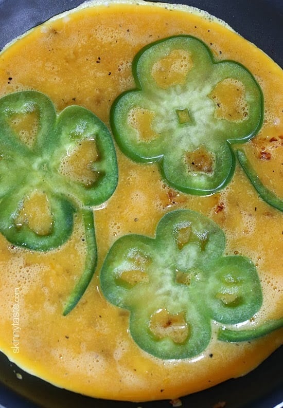Placing sliced bell peppers into shamrock shapes onto the skillet with the egg batter.