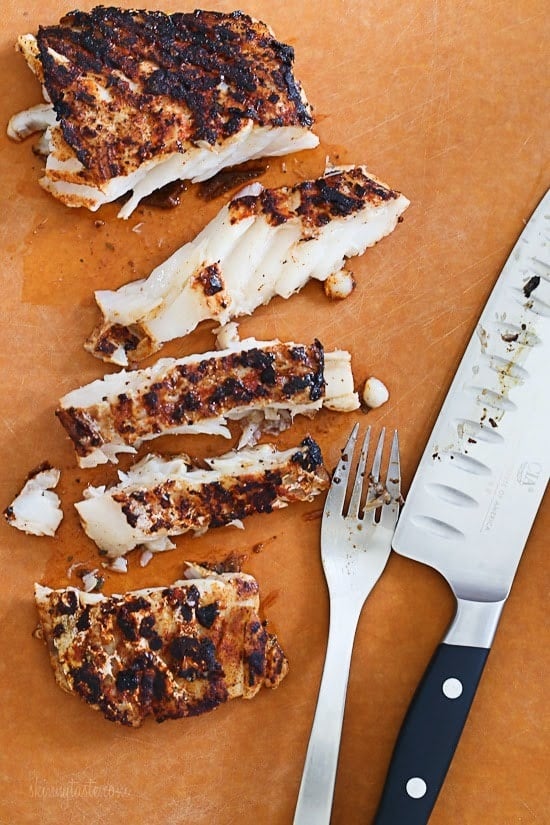 A cutting board with blackened grilled white fish cut into a few slices