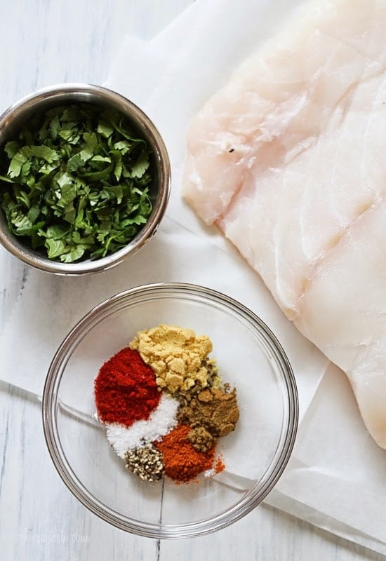 A bowl of chopped cilantro, and a bowl of mixed spices including paprika, salt, dry mustard, cumin, oregano, and black pepper