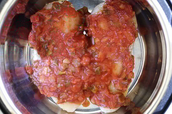 Instant Pot salsa chicken is so quick and easy! Make this juicy 2-ingredient shredded chicken to use in tacos, rice bowls, salads, and more. Two chicken breasts covered with salsa inside the Instant Pot.