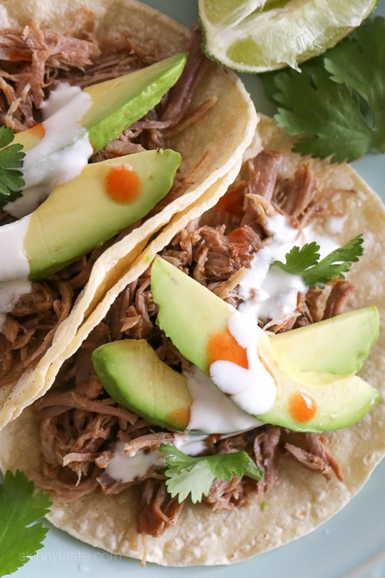 The best Instant Pot Carnitas recipe! Make juicy Mexican pulled pork in the pressure cooker for tacos, burrito bowls, taco salads, and more. Overhead view of Instant Pot carnitas tacos on a plate topped with avocado slices, cilantro, and cheese.