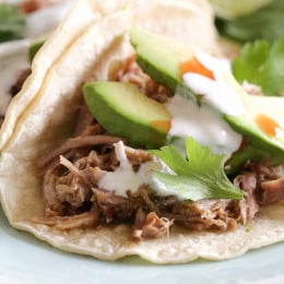Instant Pot carnitas tacos on a plate topped with avocado slices, cilantro, and cheese.