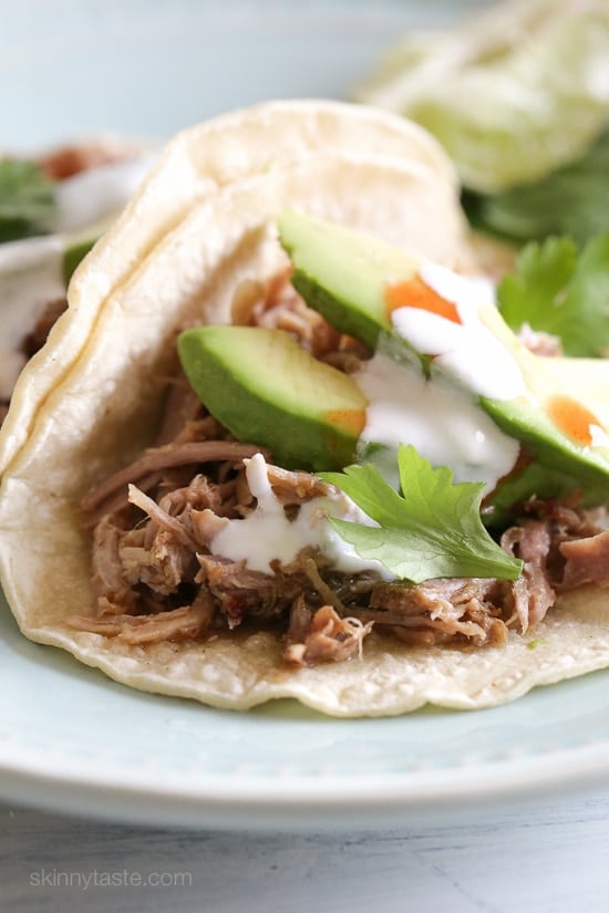 The best Instant Pot Carnitas recipe! Make juicy Mexican pulled pork in the pressure cooker for tacos, burrito bowls, taco salads, and more. Instant Pot carnitas tacos on a plate topped with avocado slices, cilantro, and cheese.