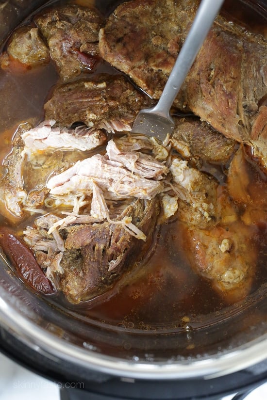 The best Instant Pot Carnitas recipe! Make juicy Mexican pulled pork in the pressure cooker for tacos, burrito bowls, taco salads, and more. A fork stuck into cooked and partially shredded pork shoulder inside the Instant Pot.