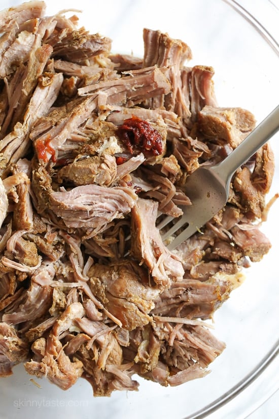The best Instant Pot Carnitas recipe! Make juicy Mexican pulled pork in the pressure cooker for tacos, burrito bowls, taco salads, and more. Instant Pot pork carnitas in a glass bowl with a fork, after shredding.