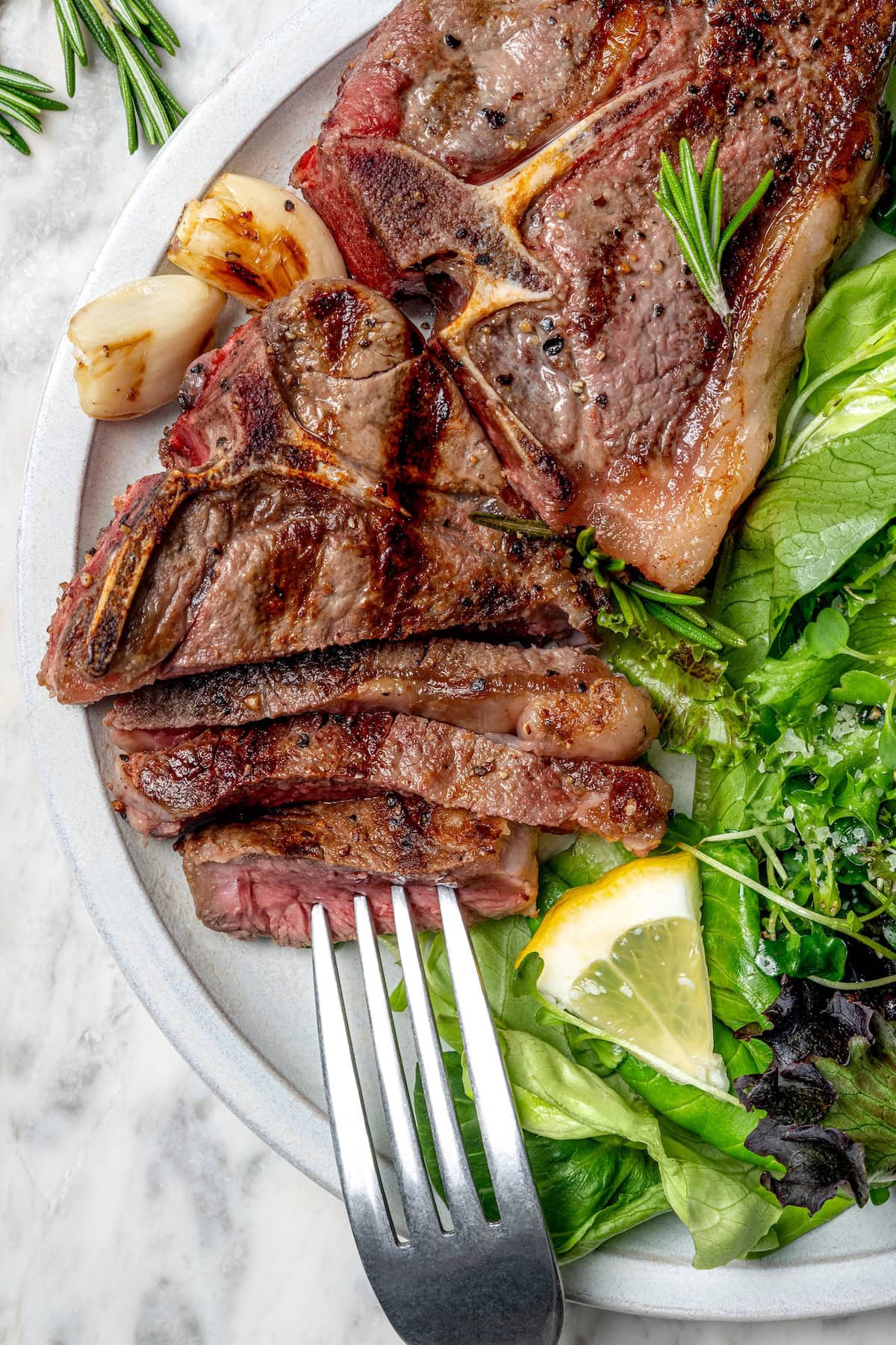 With fragrant rosemary and garlic, this easy grilled lamb chops recipe is flavorful, succulent, and one I love to cook all year long! Sliced grilled lamb chop on plate with salad and fork