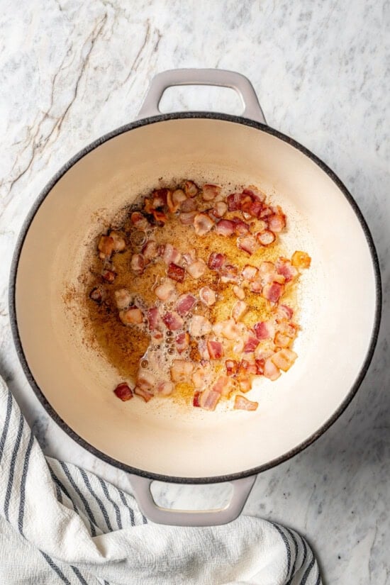 This delicious, hearty navy bean soup is inexpensive and easy to make! Cook it on the stovetop, or in your Instant Pot or slow cooker. Bacon cooking in Dutch oven