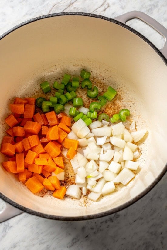 This delicious, hearty navy bean soup is inexpensive and easy to make! Cook it on the stovetop, or in your Instant Pot or slow cooker. Carrots, onion, and celery cooking in Dutch oven