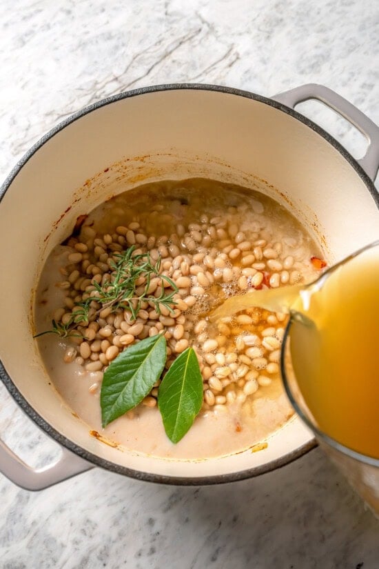 This delicious, hearty navy bean soup is inexpensive and easy to make! Cook it on the stovetop, or in your Instant Pot or slow cooker. Pouring broth into pot for navy bean soup