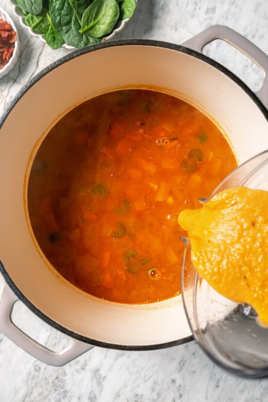 This delicious, hearty navy bean soup is inexpensive and easy to make! Cook it on the stovetop, or in your Instant Pot or slow cooker. Pouring pureed soup back into pot to thicken it