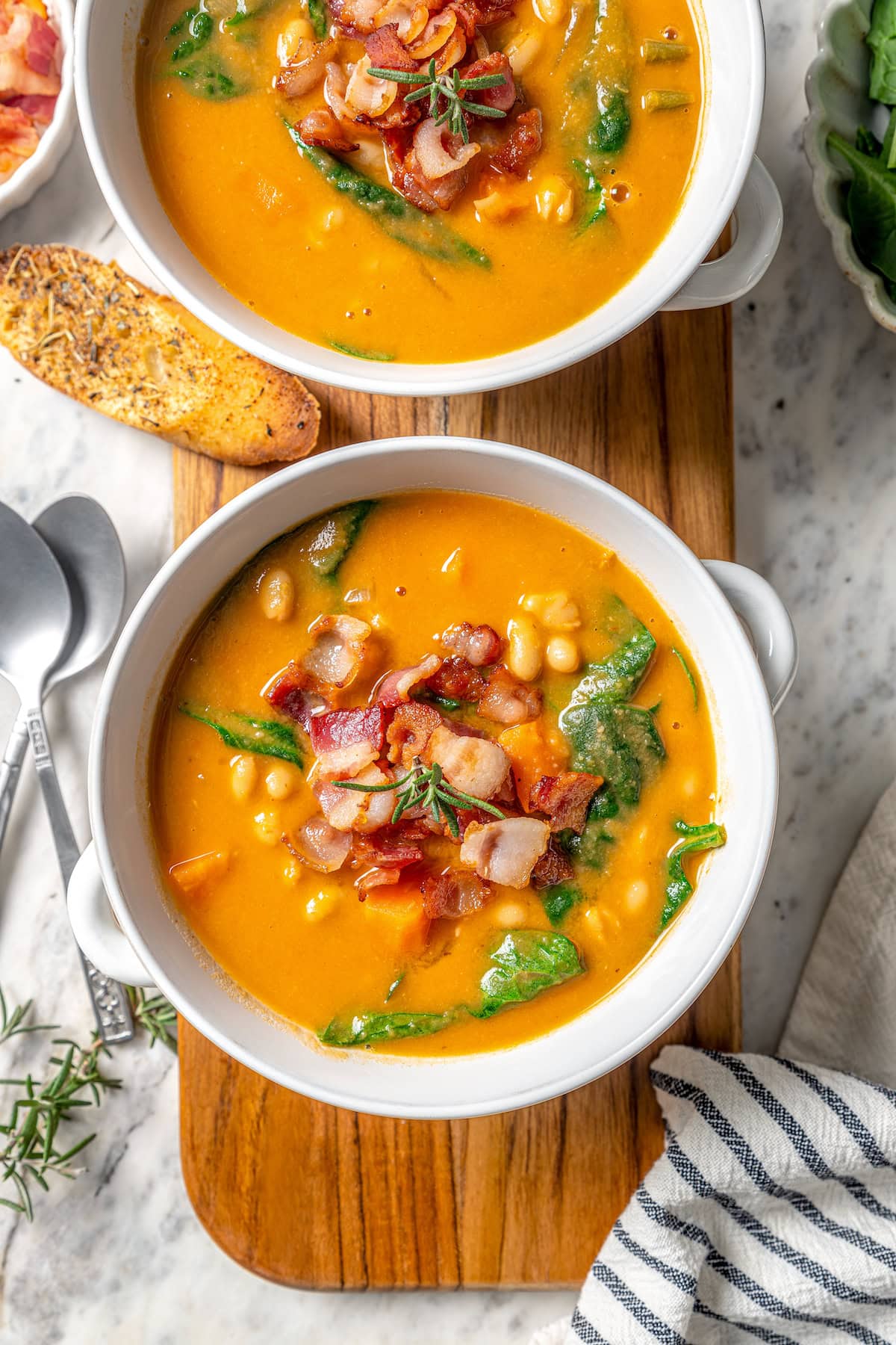 This delicious, hearty navy bean soup is inexpensive and easy to make! Cook it on the stovetop, or in your Instant Pot or slow cooker. Two bowls of navy bean soup with bacon