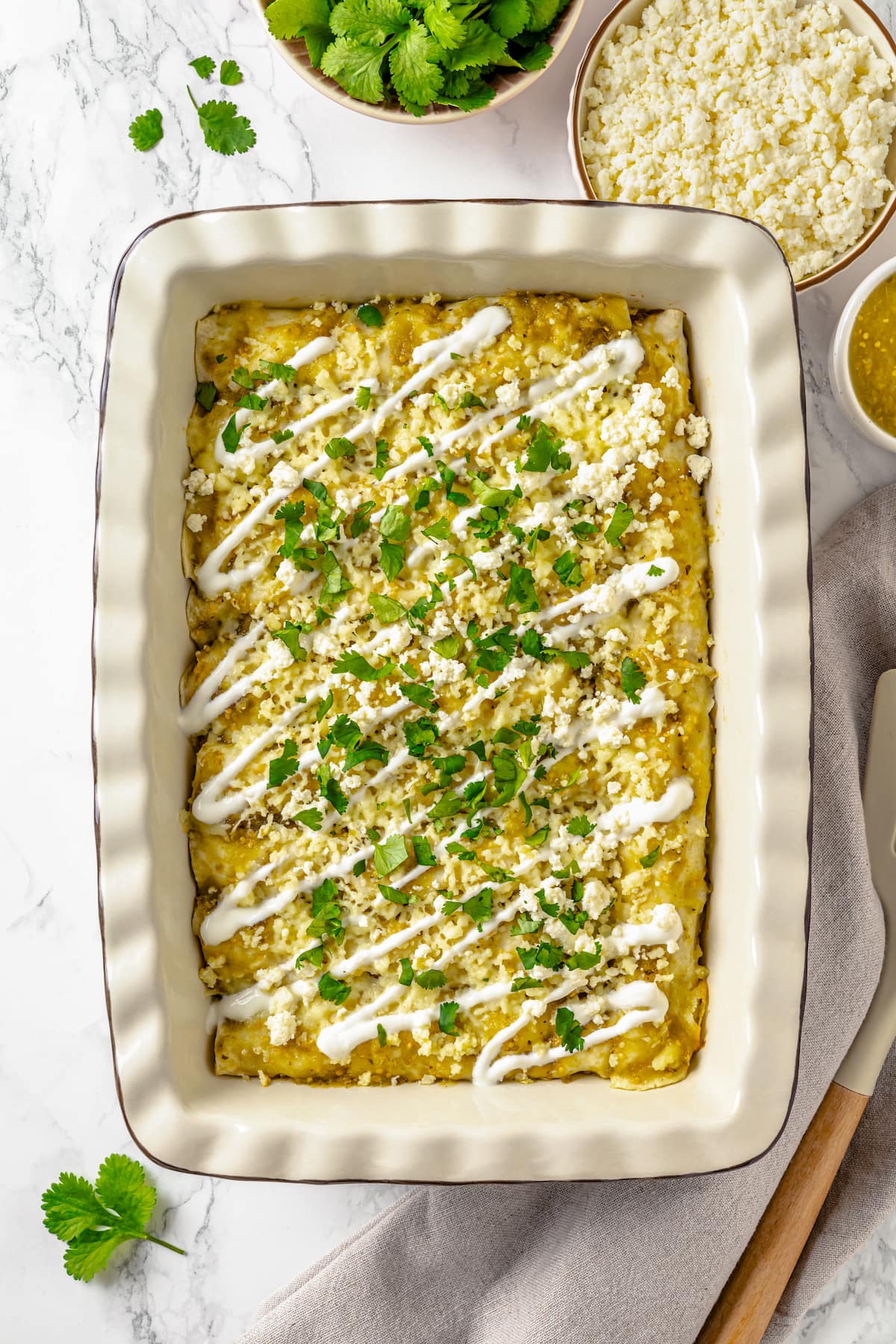 These Chicken Enchiladas Verdes (aka Green Enchiladas) are made with white corn tortillas, salsa verde, chicken breast, and queso fresco. A casserole dish of enchilada verdes topped with sour cream and cilantro