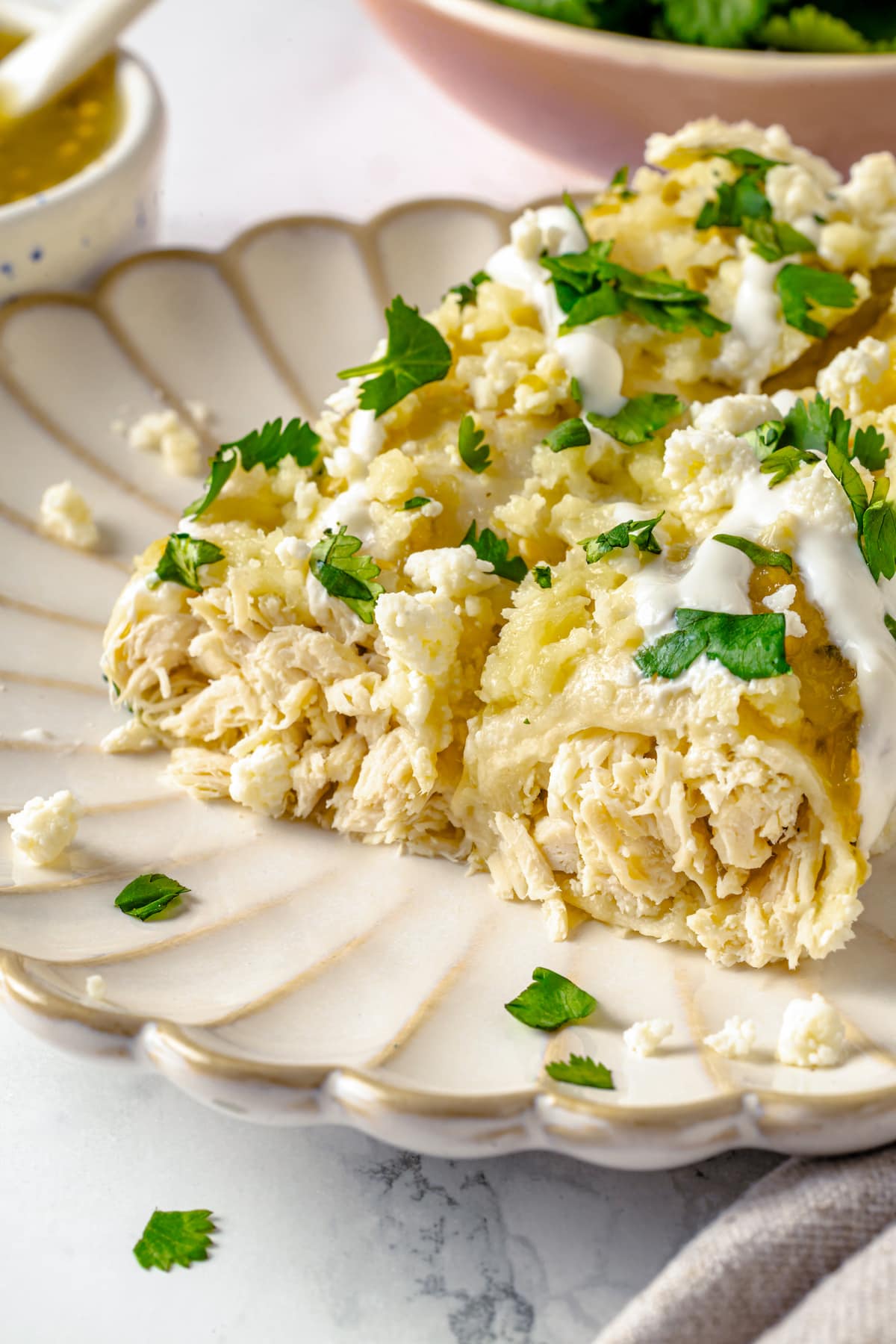 These Chicken Enchiladas Verdes (aka Green Enchiladas) are made with white corn tortillas, salsa verde, chicken breast, and queso fresco. Two green chicken enchiladas on a plate with the ends off to show the chicken inside