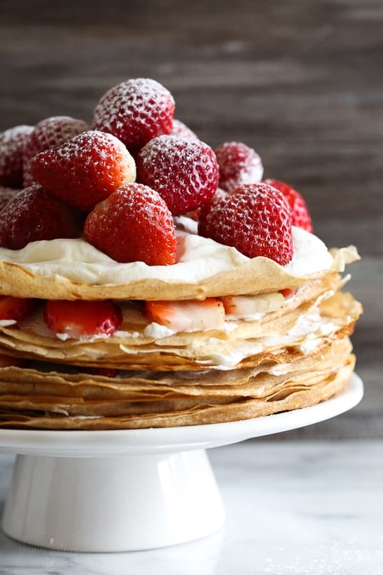 This easy strawberry crêpe cake is a light summer dessert ready to impress! A few simple swaps make it healthier than the traditional version. Strawberry crepe cake on cake stand