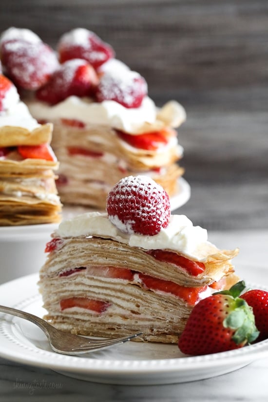 This easy strawberry crêpe cake is a light summer dessert ready to impress! A few simple swaps make it healthier than the traditional version. Slice of strawberry crepe cake on plate with fork and fresh berries