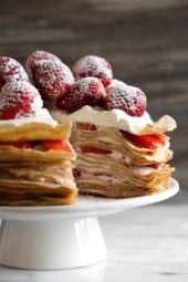 Strawberry crepe cake on cake stand with slice removed to show layers