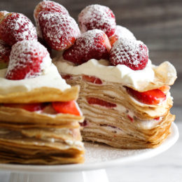 Strawberry crepe cake on cake stand with slice removed to show layers