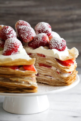 Strawberry crepe cake on cake stand with slice removed to show layers