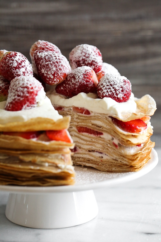 Strawberry crepe cake on cake stand with slice removed to show layers