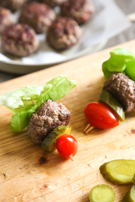 Mini burgers with bacon, layered on a bamboo skewer with lettuce, tomatoes and pickles! Who can resist your favorite foods on a stick – not me! These burger bites make the perfect low-carb appetizer to please everyone from age six to age sixty, just set out some ketchup and mustard for dipping and watch them disappear.