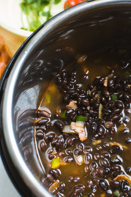 These Instant Pot Black Beans are flavored with warm spices, bacon, onion, garlic, and poblano pepper for a smoky but mild taste. Instant Pot black bean ingredients in the pressure cooker