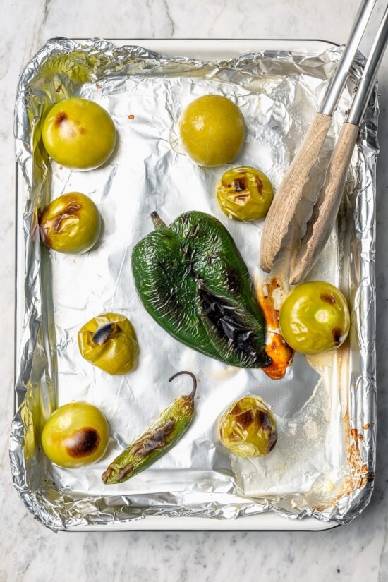 Roasting the tomatillos and peppers first makes this homemade salsa verde recipe extra delicious. Easy to make and better than store-bought! Overhead view of roasted peppers and tomatillos on foil lined pan