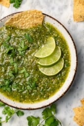 Bowl of salsa verde with 3 lime wedges and chip