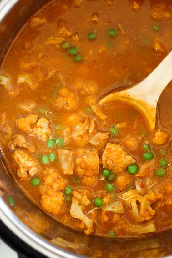 This Instant Pot Chicken Tikka Masala with cauliflower and peas is a lightened up, dairy-free version of the classic Indian curry. A wooden spoon stirring chicken tikka masala in the Instant Pot